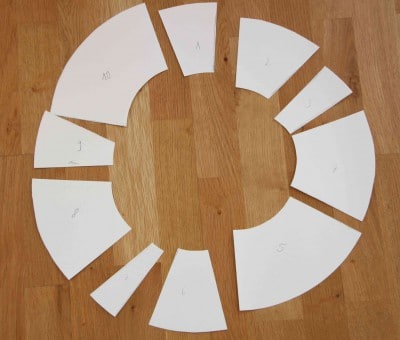 Papierteile für einen Frühlingskranz, nummeriert und auf einem Holztisch angeordnet, zum Basteln eines dekorativen Frühlingskranzes.