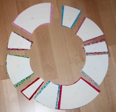 Bunte Stoffreste in verschiedenen Mustern und Farben, angeordnet in einem Kreis auf Holzboden, für einen Frühlingskranz zum Basteln oder Dekorieren.