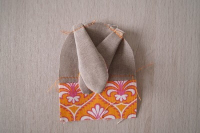 Stoffhäschen in Arbeit, mit buntem Stoffmuster und angenähten Ohren, auf einer Holzoberfläche. Perfekt für Osterdekorationen und Handarbeit.