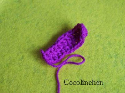Kleiner, handgestrickter Eierwärmer in Hasenform aus lila Wolle auf grünem Hintergrund, passend zum Osterfest und für kreative Osterdekorationen.