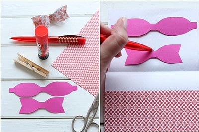 Bastelmaterialien für Osterzweig: pinke Papier-Schleifen, Schere, Kleber, Holzklammer, Musterpapier, und ein Stoffschmetterling für kreative Osterdekoration.