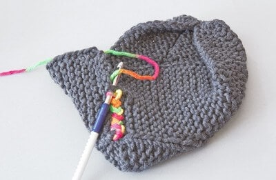 Handgestrickte graue Hausschuhe aus Wolle, perfekt für gemütliche Tage zu Hause, mit Stricknadeln und buntem Garn. Ideal für kuschelige Momente und warme Füße.