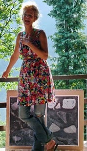 Junge Frau in buntem Blumenrock posiert vor Kunstwerken bei HANDMADE Kultur, umgeben von grüner Natur, zeigt kreative Atmosphäre und handgemachte Kunst.