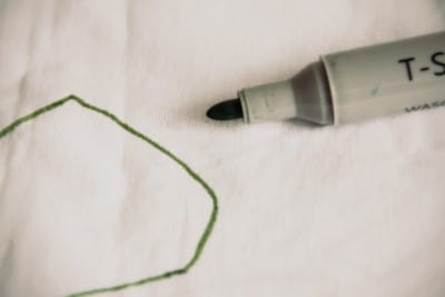 Grüner Filzstift zeichnet eine geometrische Form auf weißem Stoff, kreative Handarbeit für DIY-Projekte und textile Gestaltung bei Handmade Kultur.