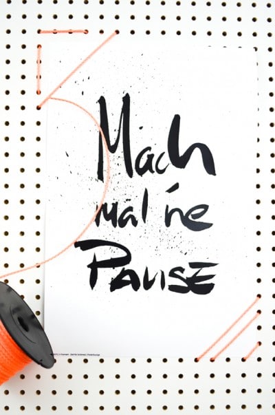 Makramee Wanddeko mit dem Schriftzug "Mach mal ne Pause" auf weißem Hintergrund, umgeben von Bastelmaterialien und Dekorationsdetails für DIY-Projekte.