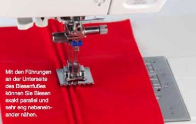 Naheaufnahme des Biesenfußes an einer Nähmaschine, der präzise Biesen in rotem Stoff erzeugt, ideal für nostalgische Nähprojekte.