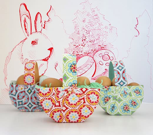Bunte Osterkörbe mit Eiern und Dekorationen, passend für Ostern, auf einer weißen Oberfläche mit Osterhasenzeichnung im Hintergrund.