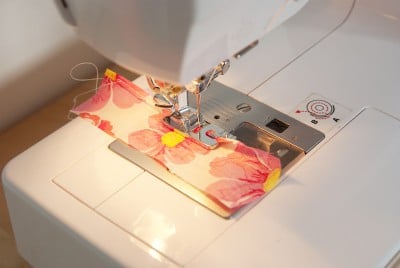Naht an einem Stoffstück mit Blumenmuster, das mit einer Nähmaschine genäht wird, für professionellen Rollsaum.