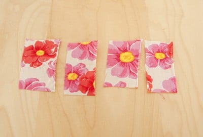 Vier Stoffreste mit Blumenmuster in Rot- und Pinktönen, die für Nähprojekte vorbereitet sind, passend zum Thema Rollsaum mit der Nähmaschine.