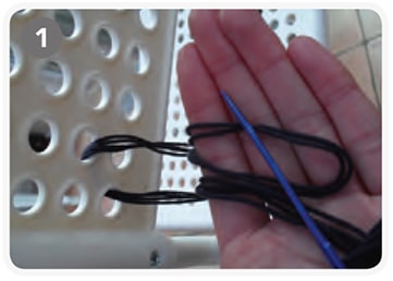 Nahaufnahme einer Hand, die mit blauer Nadel und schwarzer Schnur auf einer perforierten Oberfläche arbeitet, für handgefertigte Kreuzsticharbeiten.