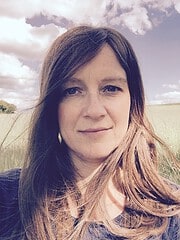 Frau mit langen braunen Haaren und natürlichem Make-up, die in einem offenen Feld steht, umgeben von Natur und Himmel, für Handmade Kultur, kreative Handwerkskunst, nachhaltiges Leben.