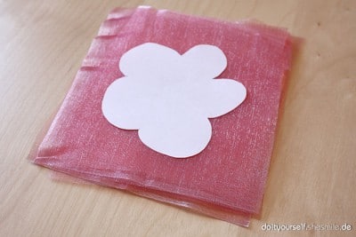 Weißes Blumenmotiv aus Papier auf rosa Organza-Stoff, für Bastel- und Nähprojekte, passend zu der Anleitung für Blumen aus Organza.