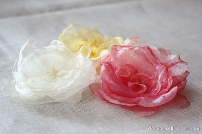 Drei handgefertigte Blumen aus Organza-Stoff in Weiß, Gelb und Rosa, ideal für Bastel- und Nähprojekte, kreative Dekorationen und Geschenkideen.