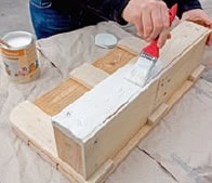Selbstgebautes Holzregal aus Paletten, das mit weißer Farbe gestrichen wird, ideal für kreative Küchen- oder Wohnideen.