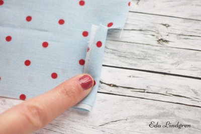 Hand zeigt das Nähen eines Wäschebeutels aus Stoff mit rotem Punktmuster auf weißem Hintergrund, geeignet für DIY Nähprojekte.