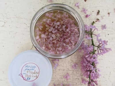 Selbstgemachtes Zuckerpeeling mit frischen Fliederblüten in einem Glas, ideal für natürliche Hautpflege und Aromatherapie.