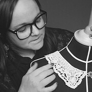 Frau mit Brille betrachtet handgefertigten Schmuck und Textilien auf einem schwarzen Stoffhintergrund, zeigt Interesse an kreativen Handwerkskunst und Design.