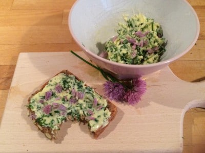 Frische Kräuterbutter mit Schnittlauch und Petersilie auf einem Holzbrett, serviert mit einer Brotscheibe, ideal für hausgemachte Butterrezepte.