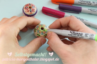 Hand beim Bemalen von dekorativen, handbemalten Möbelknöpfen mit Sharpie-Markern, kreative DIY-Deko für Möbel, handgemacht, individuelle Möbelknöpfe.