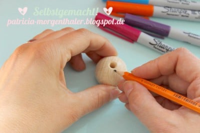 Hand beim Bemalen eines runden Holzknopfs mit einem orangefarbenen Marker, kreative DIY-Bastelarbeit für Möbeldekoration.