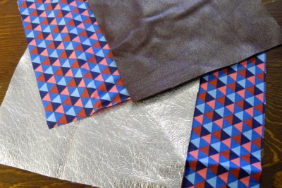Verschiedene Stoffe und Leder für handgemachte Lederwaren, inklusive bunter geometrischer Stoffe, schwarzes Leder und silbernes Material, ideal für kreative Näharbeiten.