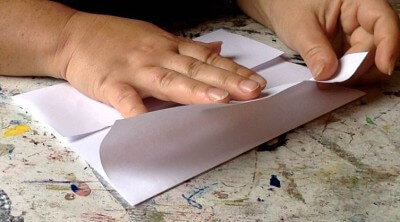Person falzt und faltet Papier, um eine Sammelmappe zu basteln, ideal für kreative Handarbeiten und Scrapbooking-Projekte.