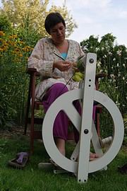 Frau beim Spinnen mit einer Handspindel im Garten, umgeben von Blumen und Natur, zeigt traditionelles Handwerk und kreative Handarbeit für nachhaltige Kultur.