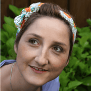 Junge Frau mit buntem Haarband, die kreative Handarbeit in einem Garten zeigt, symbolisiert die Vielfalt und das Engagement für handgemachte Kultur und Kunsthandwerk.