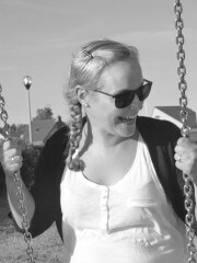 Lächelnde Frau mit Sonnenbrille schaukelt im Park, umgeben von Bäumen und Himmel, bei schönem Wetter, Freizeit und Natur genießen.