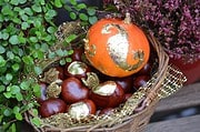 Kreative Herbstdekoration mit einem bemalten Kürbis, goldenen Akzenten, Kastanien, und frischen Blumen in einem Korb, ideal für saisonale Handwerkskunst.