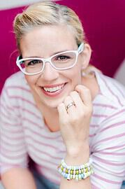 Lächelnde Frau mit weißen Brille, trägt gestreiftes Shirt und bunte Armbänder, vermittelt Freude und Kreativität im Kontext von Handmade Kultur.