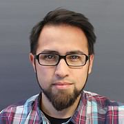 Mann mit dunklem Haar, Brille und Bart trägt kariertes Hemd, blickt direkt in die Kamera, professionelles Porträt für Handmade Kultur.