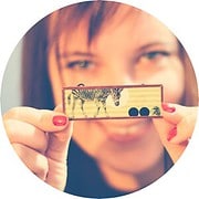 Frau hält ein kleines, handgefertigtes Kunstwerk mit Tiermotiven, das die kreative Vielfalt und das handwerkliche Können bei HANDMADE Kultur zeigt.