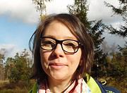 Frau mit Brille und Rucksack in natürlicher Umgebung, die an Handmade Kultur interessiert ist, umgeben von Bäumen und Himmel, ideal für kreative Handwerkskunst und Kulturveranstaltungen.