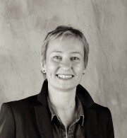 Lächelnde Frau mit kurzen Haaren, dunklem Blazer und Hemd, professionell und freundlich, für Handmade Kultur Website.