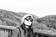 Frau mit Sonnenbrille und Mütze auf einer Holzbrüstung, umgeben von einer malerischen Berglandschaft, Fokus auf Natur und Handwerkskunst.