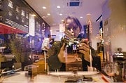 Reflexion einer Person beim Fotografieren in einem Café mit Blick auf die Stadt, kreative Atmosphäre, urbanes Handwerk, Kunst und Kultur, handgemachte Produkte.