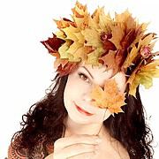 Frau mit dunklen Haaren trägt eine Krone aus buntem Herbstlaub und trägt ein herbstliches Kleid, strahlt Ruhe und Naturverbundenheit aus.