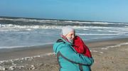 Ein Kind in warmer Jacke und Mütze steht am Strand, umgeben von Wind und Wellen, genießt die Meeresatmosphäre bei kühlem Wetter.