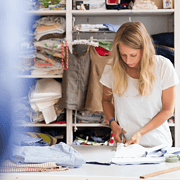 Frau beim Zuschneiden von Stoffen in einem Nähatelier, umgeben von Stoffen, Nähzubehör und kreativen Materialien, Fokus auf Handarbeit und Textilkunst.