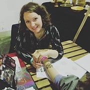 Frau bei HANDMADE Kultur zeigt handgemachte Tätowierungen, umgeben von Bastelmaterialien und Kunstwerken, in einem kreativen Workshop für handgemachte Kunst.