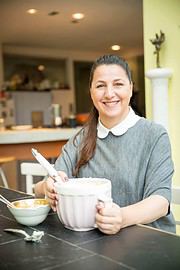 Frau beim Backen mit einem Handmixer in einer modernen Küche, lächelnd, kreative Handarbeit, hausgemachte Backwaren, gemütliches Ambiente, DIY-Kultur.