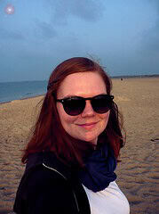 Frau mit Sonnenbrille und Schal am Strand, symbolisiert kreative Handwerkskunst und Entspannung bei Handmade Kultur Veranstaltungen.