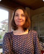 Frau mit braunen Haaren und floral gemustertem Kleid, die kreative Handarbeit bei HANDMADE Kultur präsentiert, in einem gemütlichen Raum mit natürlichem Licht.