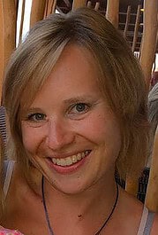 Fröhliche Frau mit blondem Haar und freundlichem Lächeln, umgeben von Holzstühlen, passend für Handmade Kultur und kreative Handwerkskunst.