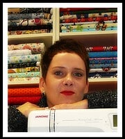 Frau mit kurzen Haaren vor Stoffregal, das bunte Stoffe für Handarbeit und Nähprojekte zeigt, bei HANDMADE Kultur, Fokus auf kreative Textilkunst und DIY-Handwerk.