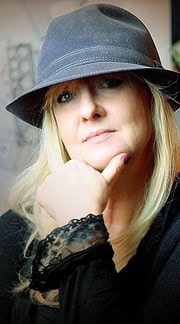 Frau mit grauem Hut und blondem Haar, die nachdenklich wirkt, als Symbol für kreative Handwerkskunst und individuelle Mode bei Handmade Kultur.