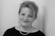 Schwarz-weiß Porträt einer Frau mit kurzen, gestylten Haaren, Perlenkette und freundlichem Lächeln, geeignet für kreative und handgemachte Kulturthemen.