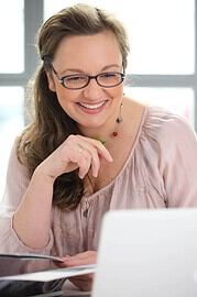 Frau mit Brille und buntem Schmuck, die kreativ an einem Projekt arbeitet, symbolisiert Handmade Kultur und kreative Handwerkskunst.