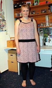 Frau trägt ein elegantes, handgemachtes Kleid mit schwarzen Akzenten, in einem kreativen Atelier mit Bastelmaterialien im Hintergrund, perfekt für Handmade Kultur.